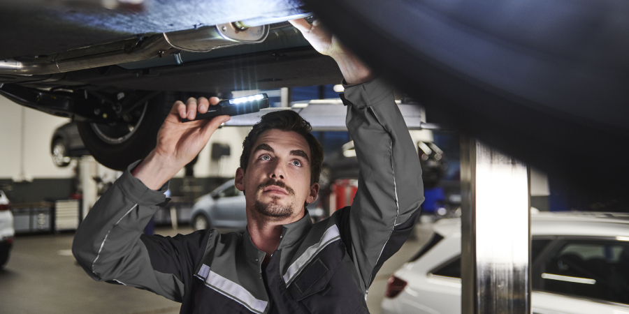 Mechaniker arbeitet unter einem Auto mit einer Taschenlampe in einer Werkstatt.