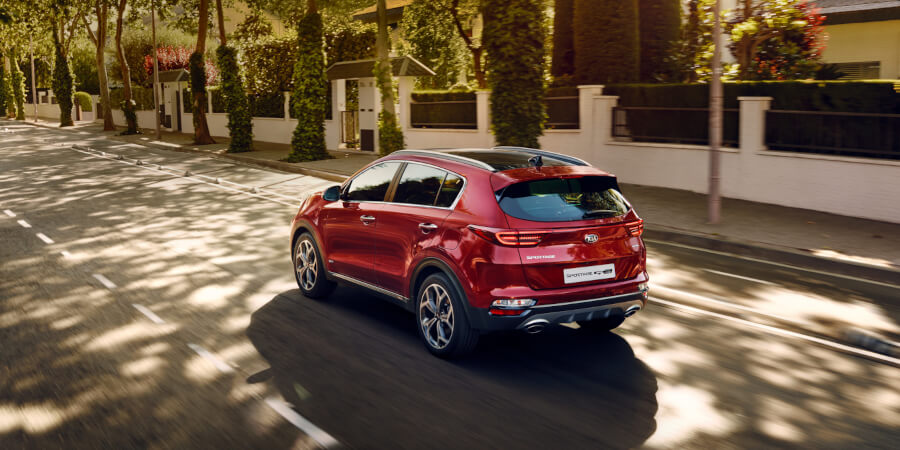 Ein rotesSUV fährt auf einer von Bäumen gesäumten Straße in einer Stadt mit Wohnhäusern im Hintergrund.